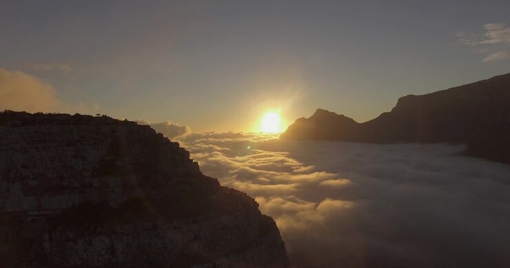 Toma de dron durante el amanecer sobre la Montaña de la Mesa y la Montaña Cabeza de León en Ciudad del Cabo, Sudáfrica, con nubes en el valle en una mañana soleada LOG