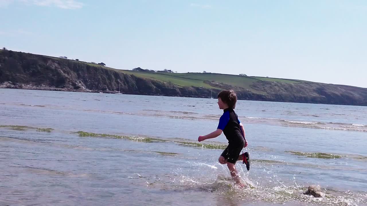 una cámara lenta, una toma panorámica de un niño corriendo por la playa, navegando lejos de la cámara en un buen día