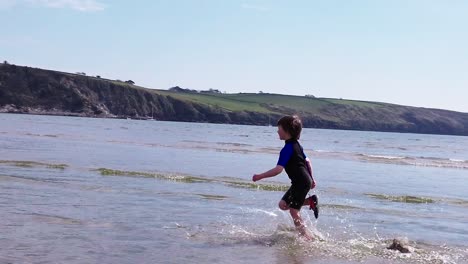 A-slow-motion,-wide-shot-of-a-young-boy-running-across-the-beach-surf-away-from-camera-on-a-fine-day