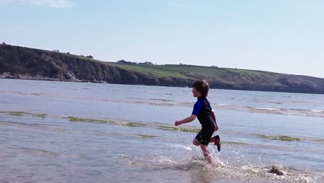 a slow motion, wide shot of a young boy running across the beach surf away from camera on a fine day