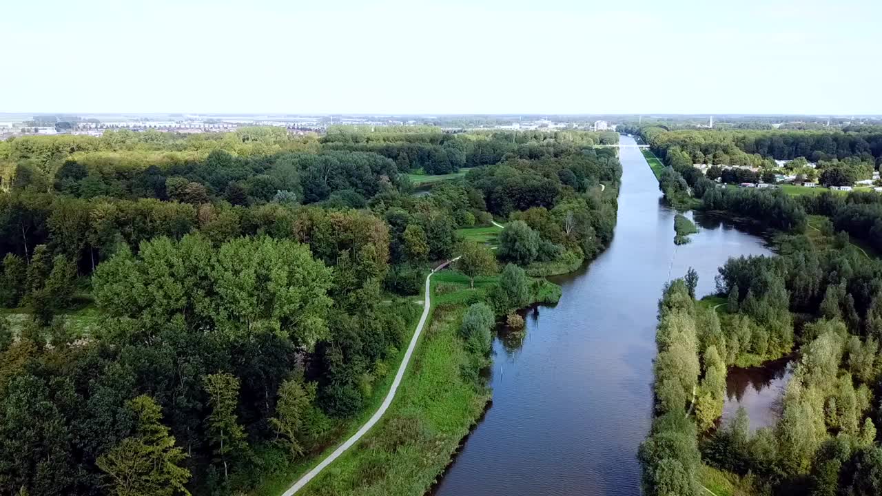 Drone che sorvola il canale nella foresta con un villaggio sullo sfondo.