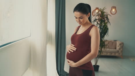 Pregnancy-and-motherhood.-Young-happy-pregnant-woman-holding-belly-at-home.