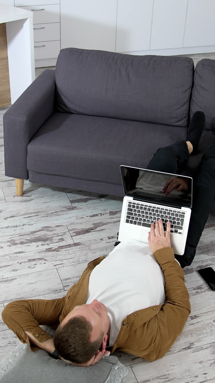Kyiv, Ukraine, 2 May 2025: Man lying in living room. Young man using laptop while lying on floor at home. Vertical video