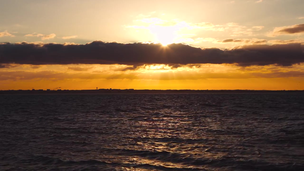 Golden sunset over rough coastal waters as clouds slowly cover the evening sun