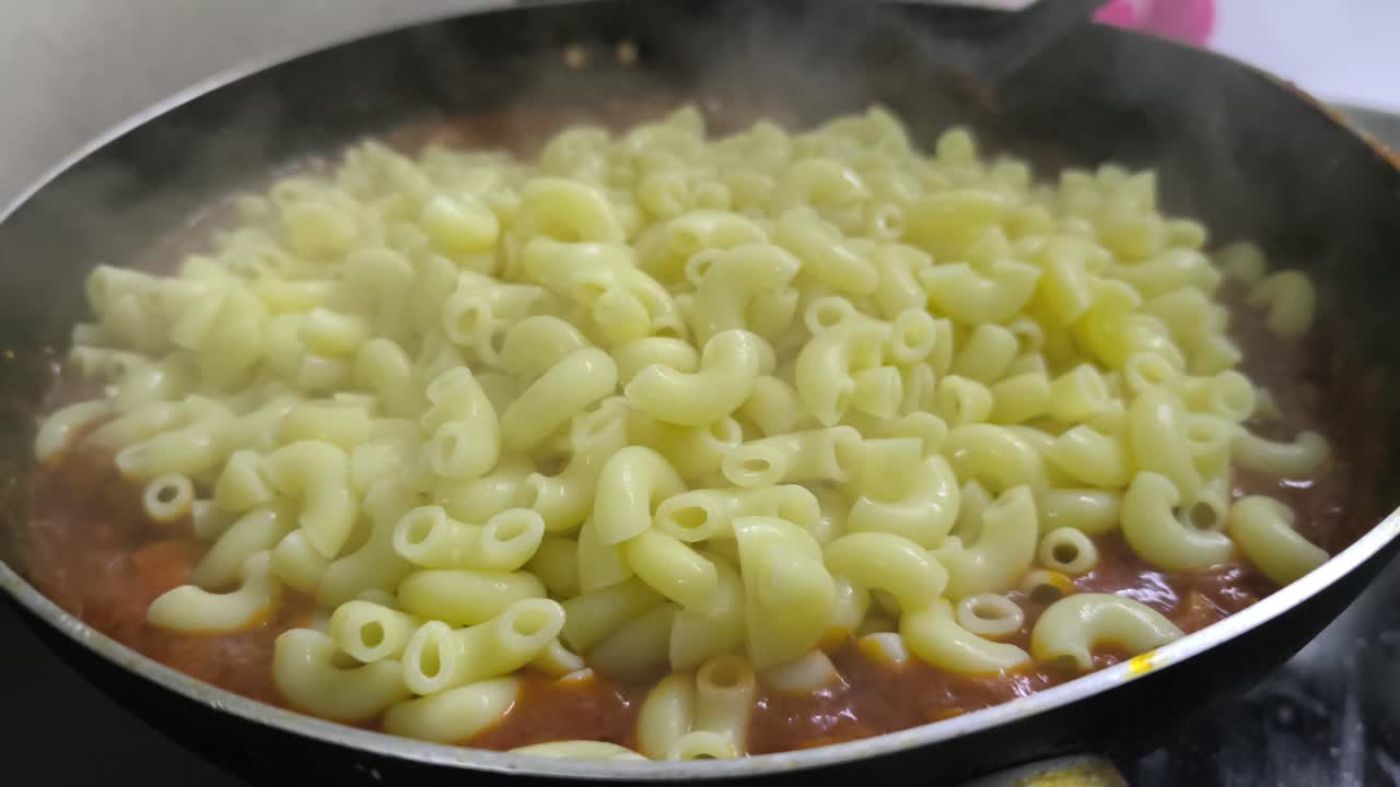 A chef is cooking macaroni in a pan, mixing it with a pre-made sauce. The bubbling mixture looks delicious and appetizing. This preparation highlights the cooking process
