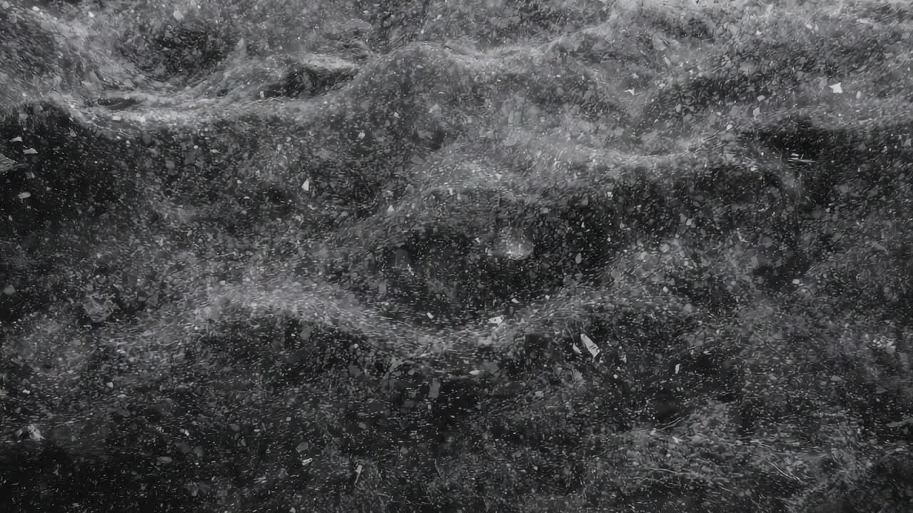 Falling fine particles settling on rippled dark surface at close-up, creating speckled texture