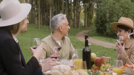 group of happy friends talking together while sitting at table during an outdoor party in the park