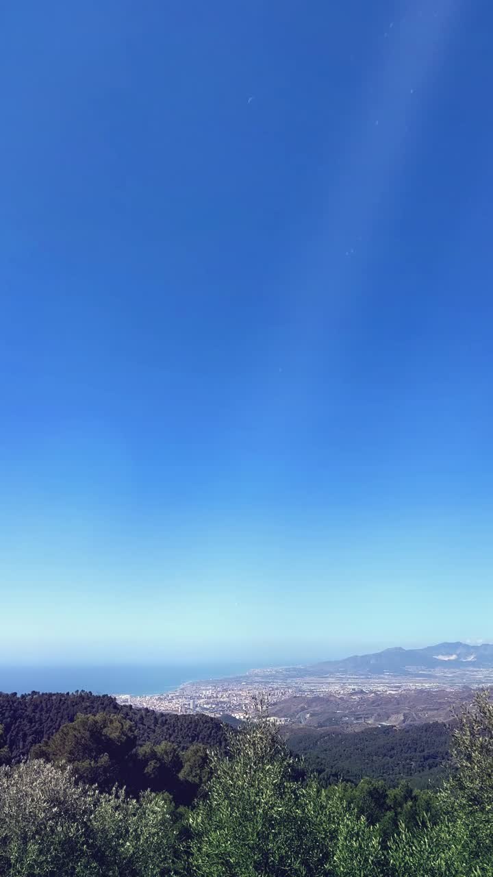 Vista panorámica de una ciudad costera, un bosque y el océano bajo un cielo azul