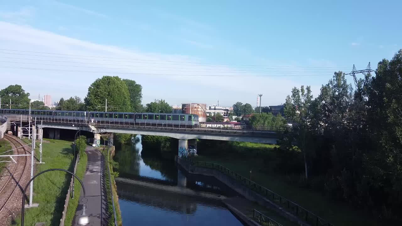 Italian subway rides over bridge and small canal, aerial ascend view