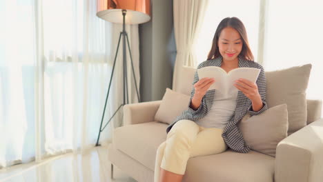 smiling young asian woman reading a book in a brightly lit contemporary living room