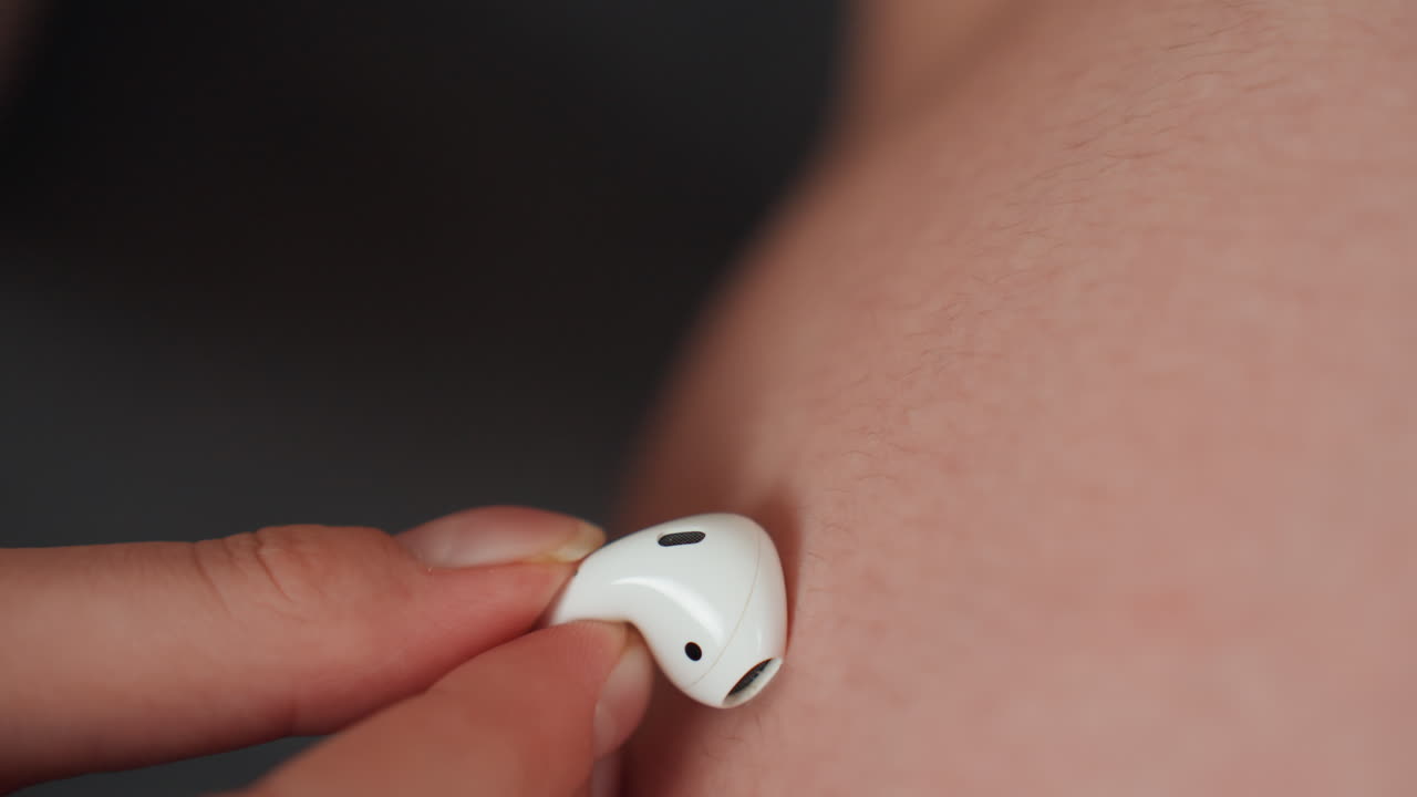 Nahaufnahme eines schwangeren Bauches mit angedrücktem Ohrhörer, sanfte Fingerspitze hält weißen Ohrhörer an warme Haut in sanft beleuchteter häuslicher Umgebung, zärtliche pränatale Bindung, angedeuteter Herzschlag und beruhigende Musik, ruhig, intim