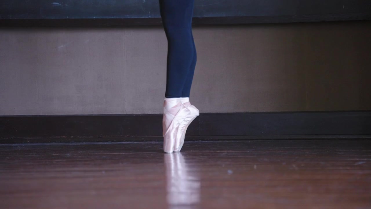 Gros plan sur une femme en collants, portant des chaussons de pointe et pratiquant le travail des pieds.