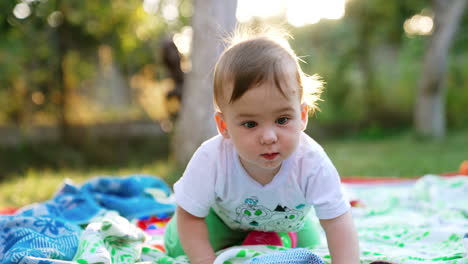 cute little toddler crawling by the plaid laid on the ground in the garden. curious beautiful child looks around with interest. blurred backdrop.