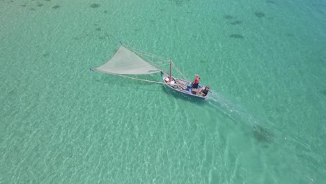 Toma-Aérea-De-Un-Pescador-Tradicional-De-Camarones-En-Un-Pequeño-Bote-De-Madera-Pescando-Camarones-En-Aguas-Claras-En-Tailandia