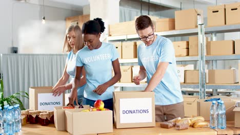 multiethnic group of volunteers in facial mask packing boxes with food in charity warehouse