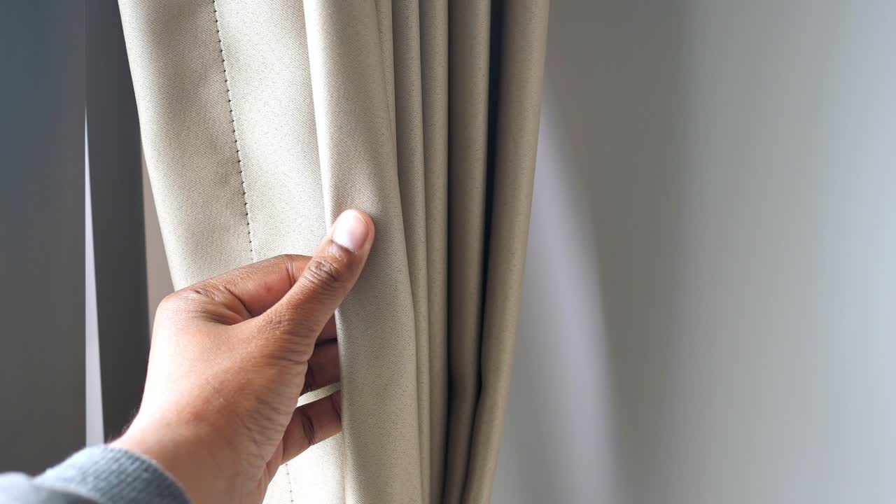 Person öffnet einen beigen Vorhang