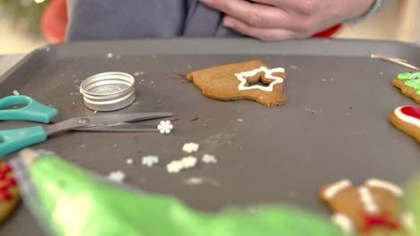 Schließen-Sie-Oben-Auf-Den-Händen-Der-Frau,-Die-Einen-Stern-Auf-Lebkuchenplätzchen-Zeichnet,-Unter-Verwendung-Eines-Spritzbeutels-Mit-Weißer-Zuckerglasur-4k