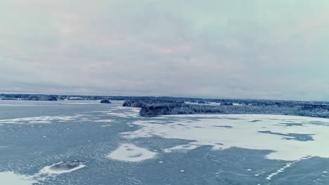 aerial backward moving shot of frozen blue lake with pattern underwater in beautiful winterscape on a cloudy day