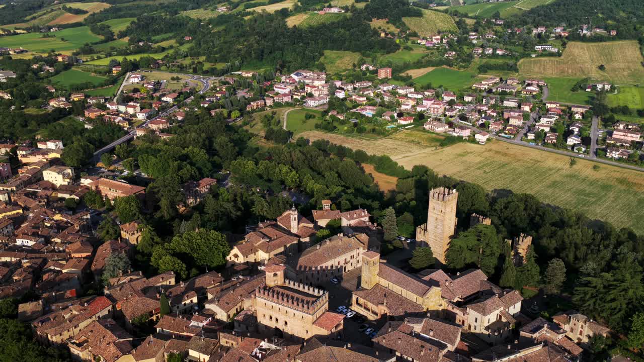 Aerial view of Castell'Arquato, a medieval village in Emilia Romagna, Italy, surrounded by picturesque hills, bathed in warm golden sunlight. Pull back, tilt up
