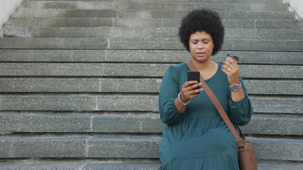 Happy plus size biracial woman using smartphone and drinking coffee