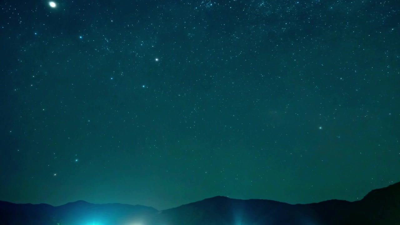 暗い山のシルエットと遠くの谷の明かりの上で輝く星々と天の川の穏やかな4K夜間タイムラプス。天文学、旅行、自然、そして穏やかな風景のテーマに最適です。