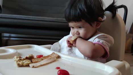 asian cute baby girl eating her homemade food on baby feeding chair