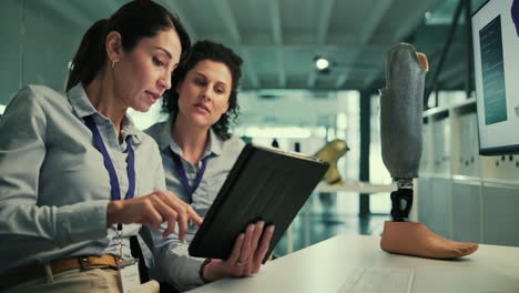 dos mujeres en una reunión en una oficina, discutiendo una pierna protésica en un escritorio