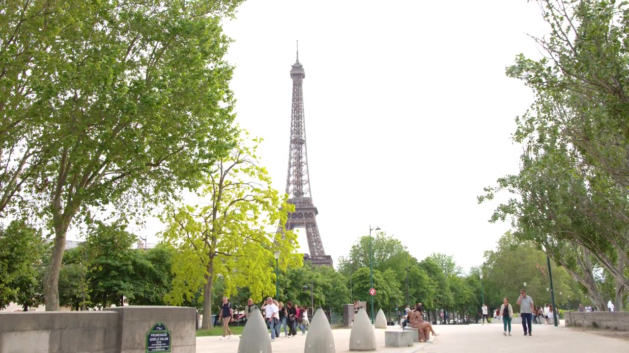 Ampia inquadratura di persone che camminano in un parco parigino con la Torre Eiffel al centro