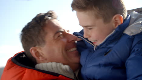 Father-lifting-son-outdoors,-both-in-warm-clothing,-close-up