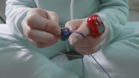 woman's hands knitting with needles. red tally counter is on finger and woman press button to count tally.