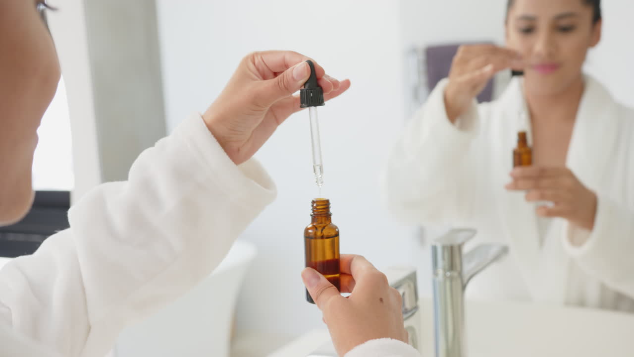 Using dropper bottle, asian woman applying skincare serum in bathroom mirror reflection, at home