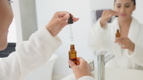 using dropper bottle, asian woman applying skincare serum in bathroom mirror reflection, at home