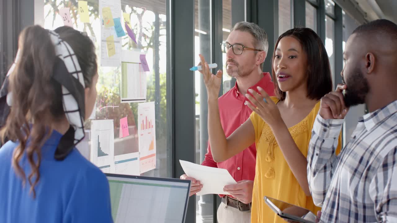 아프리카계 미국인 사업가 여성 이 사무실 창문 에 있는 메모 메모 를 통해 동료 들 과 논의 하고 있다