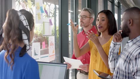 mujer de negocios afroamericana discutiendo con sus colegas sobre notas en la ventana de la oficina