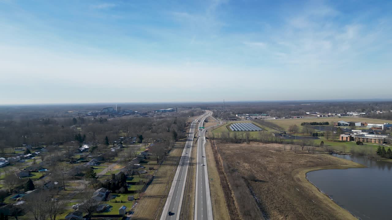 오른쪽에 작은 호수, 태양광 패널, 대학이 있는 2차선 고속도로 위를 비행하는 드론