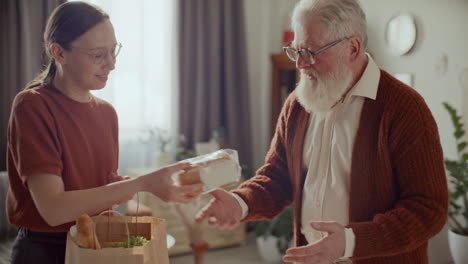 young woman delivering groceries to elderly grandfather at home