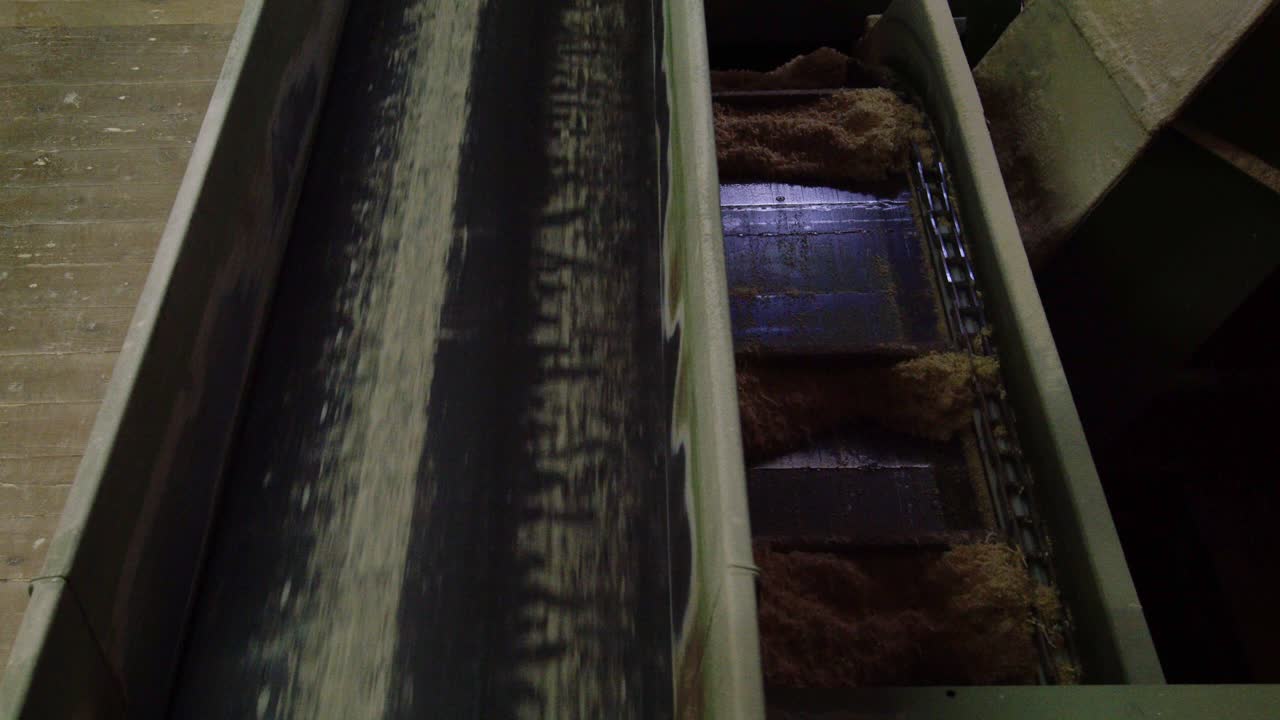 A close-up of industrial chain and belt conveyors transporting sawdust and wood fibers. This raw material, a byproduct of logging, is moved for recycling or further processing