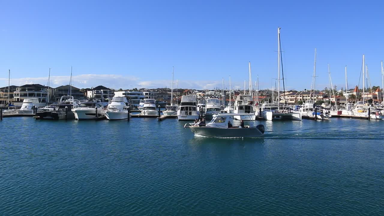 Motoscafo che procede lentamente oltre una fila di yacht a Mindarie Marina.