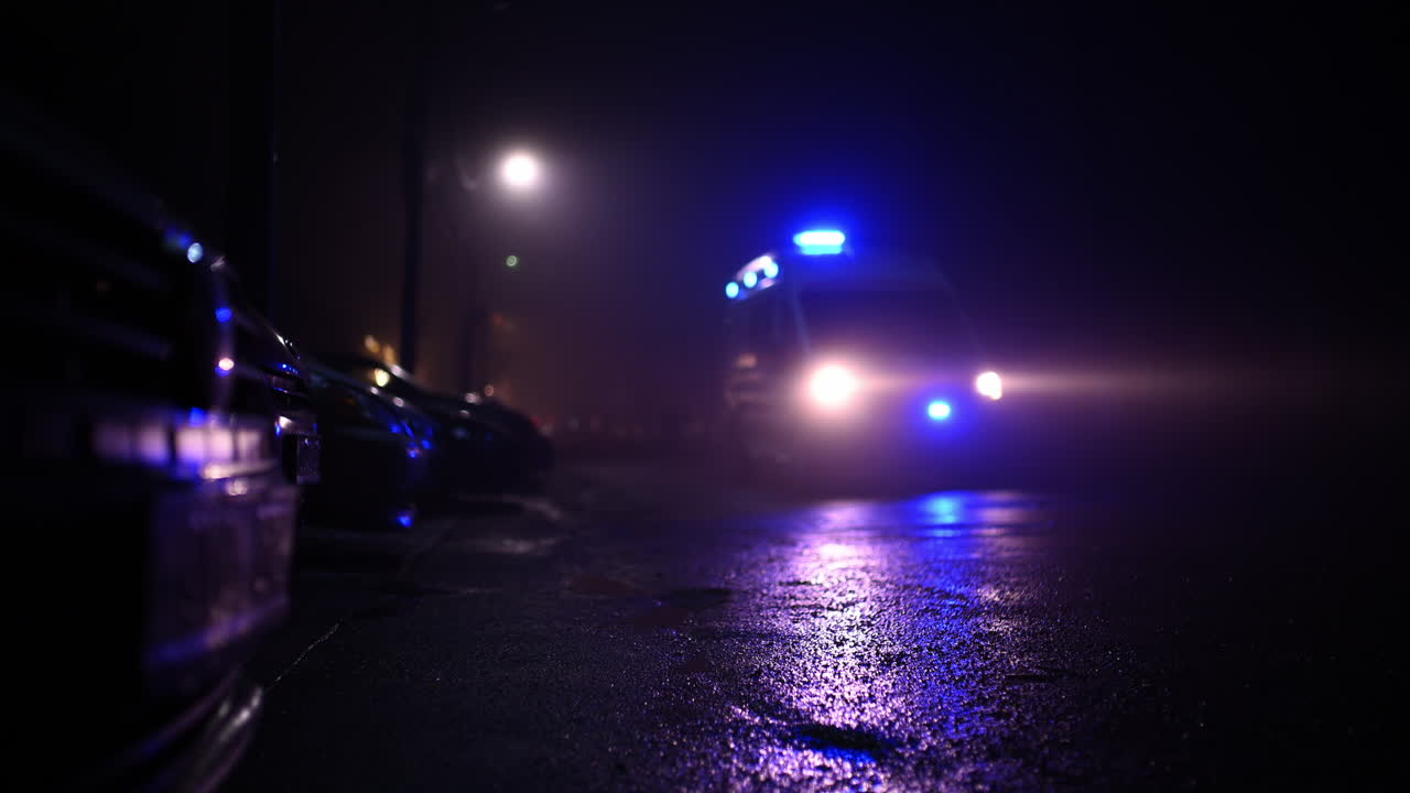 Low angle view of an emergency vehicle approaching along a dark, wet street at night