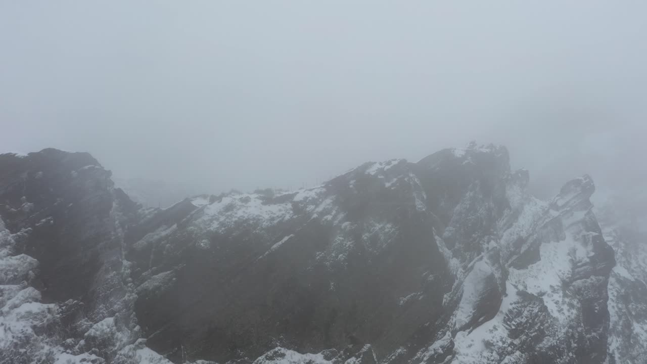 tiro de dron de ninho da manta en madeira, volando hacia adelante junto al borde del acantilado en la misteriosa y oscura tormenta de nieve