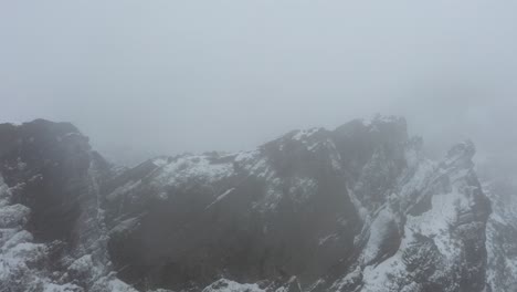 drone shot of ninho da manta in madeira, flying forwards alongside the edge of the cliff in the mysterious and dark snowstorm