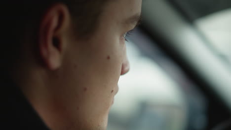 Side view of young male focused on road as he drives through urban street, background blurred with passing cars and traffic creating dynamic motion and highlighting driver concentration in cabin