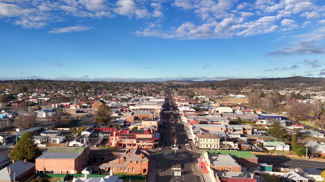 Drone footage glides above Glen Innes’ main street, revealing urban layout, residential buildings, and traffic under bright daylight with scattered clouds