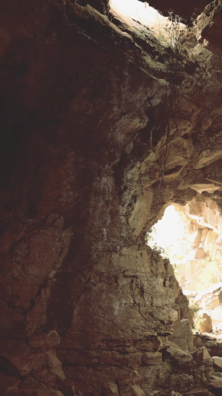 Apertura di una grotta con luce che filtra in un paesaggio roccioso.