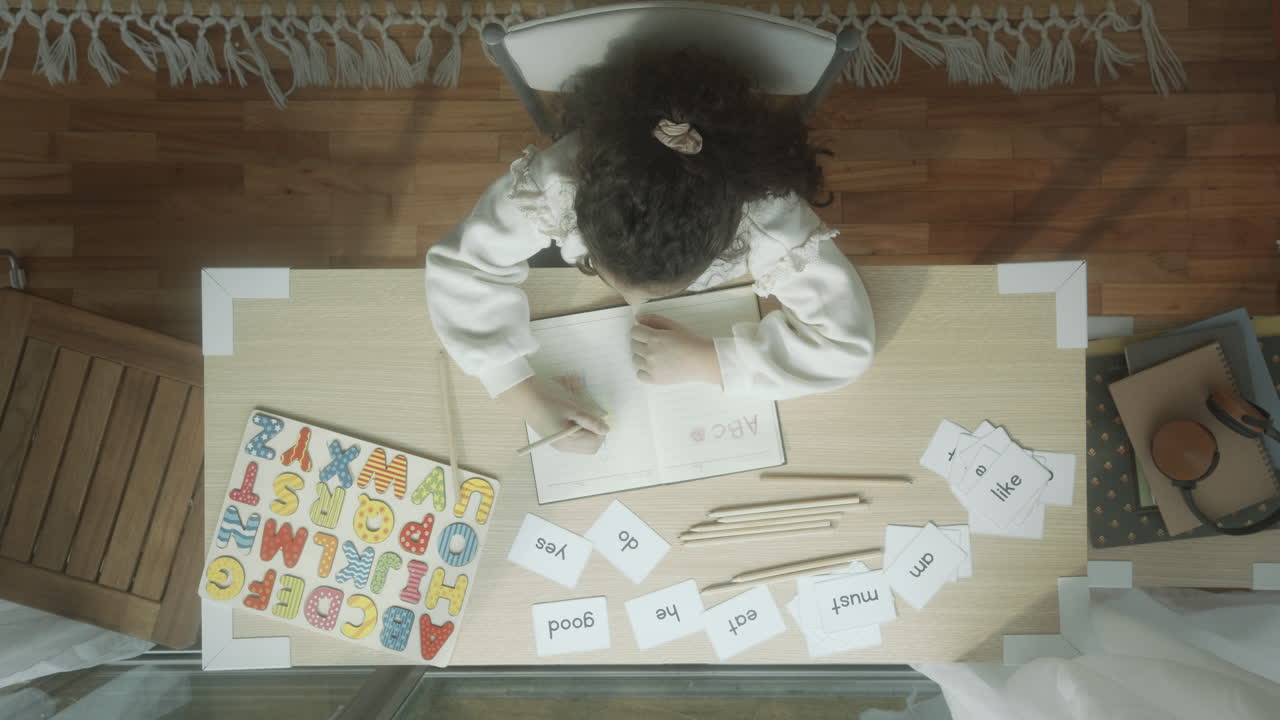 Little Girl Drawing in Notebook and Learning Alphabet at Desk