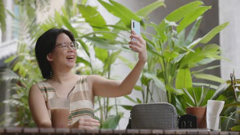 female tourist short hair wearing glasses sitting in greeting too smartphone family and having fun selfies in coffee shop. women feel relaxed and happy long weekend activities.