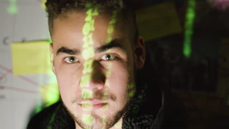 young male hacker turning head and looking at camera with binary code reflection on his face