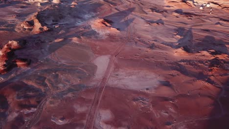 vista aérea cinematográfica de pájaros de la persona que conduce un vehículo en una carretera plana y polvorienta del desierto bajo la luz del sol del atardecer