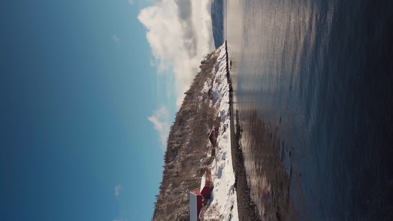 Vertical - Cabin On Snowy Mountain By The Shore Of Fjord In Trondelag, Norway During Winter