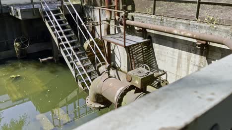 Antigua-Zanja-Industrial-Con-Tuberías-Oxidadas-Y-Viejas-Escaleras-De-Metal-Se-Ha-Inundado-De-Agua-Y-Está-Vacía-En-El-Parque-Paisajístico-Duisbrug-Nord-En-Alemania